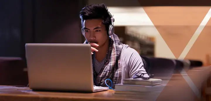 Student in the library with headphones looking at laptop 