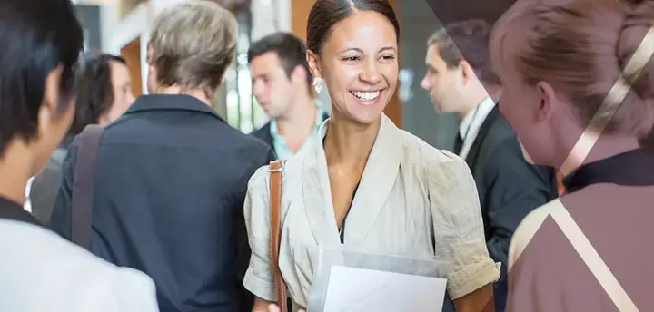 Portrait of two smiling adults holding files and talking, standing in crowded lobby 