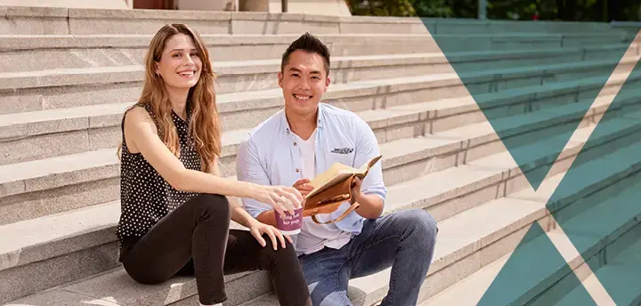 Two students sitting on steps, holding a coffee and notebook