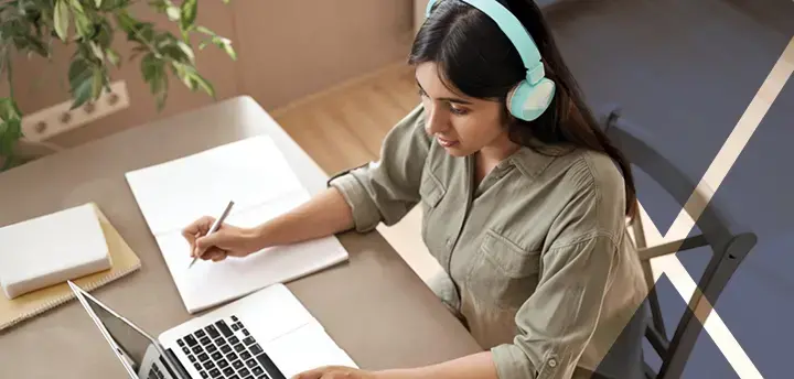 Female student wearing headphones, looking at laptop computer and learning online.